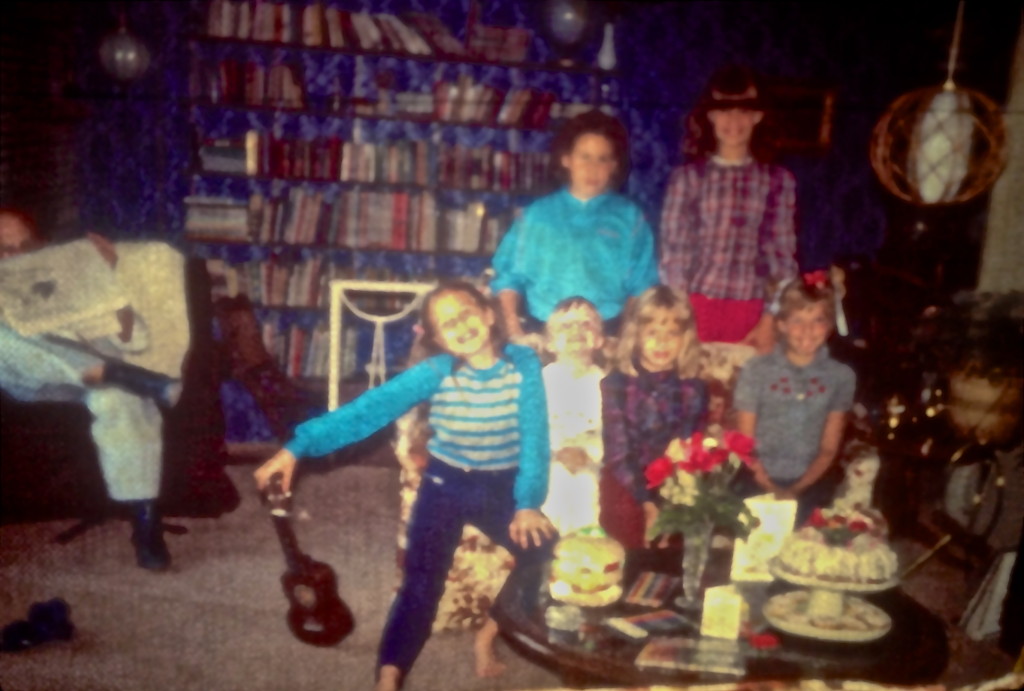 A picture taken moments before the end of the party. That's my sister with the ukelele, and I am on the right side with the red bow stuck to my head, You can see my mom's  chocolate bundt cake as well as the crystal bud vase with roses from the garden. It looks like my presents were markers and pencil crayons plus a very large hamburger coin bank, which I loved.  One other note: Michelle, the tall one in the back, is wearing red pants borrowed from my mother since her white ones got soaked with  balloon water.